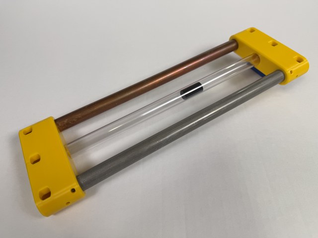 Triple-tube Lenz’s law demonstrator with copper, clear, and aluminum tubes held by yellow end caps.